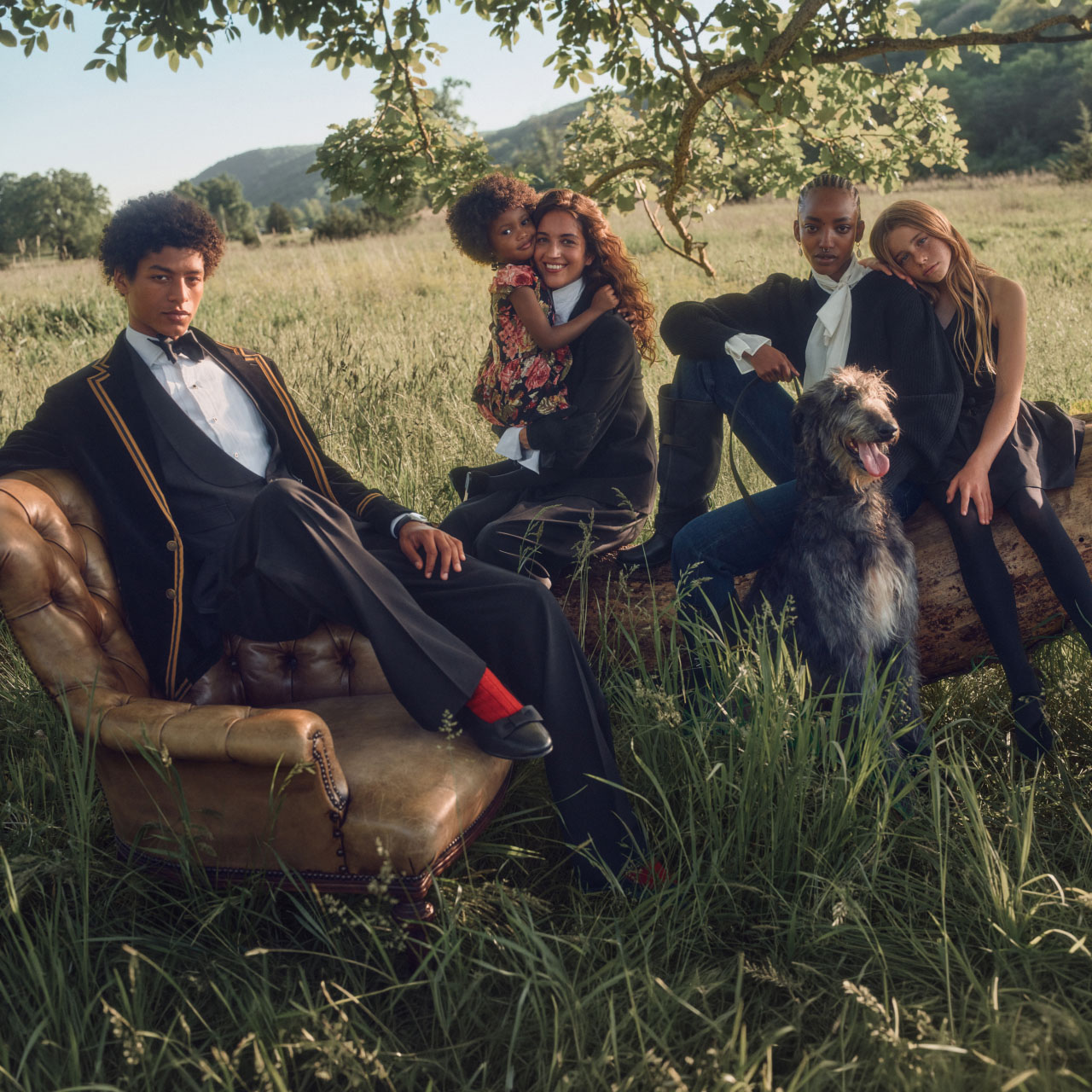 Group of five people in formal navy and black blazers posed outdoors in countryside setting with terrier dog