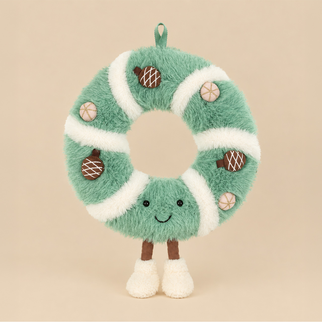 Festive Jellycat wreath plush toy with green fuzzy body, white trim, decorative pinecones, and smiling face