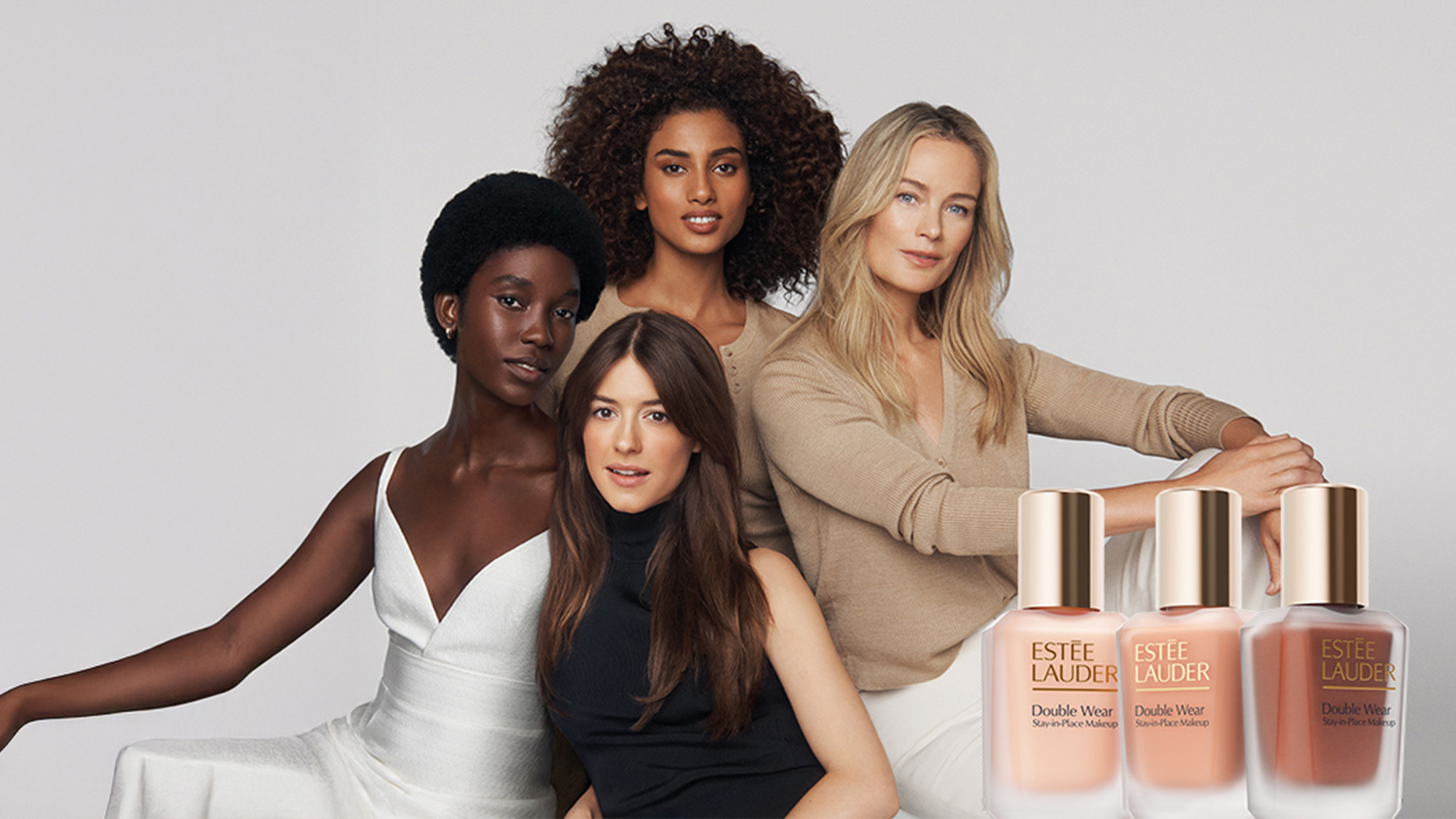 Four women pose with Estée Lauder foundation bottles, set against a light gray background.