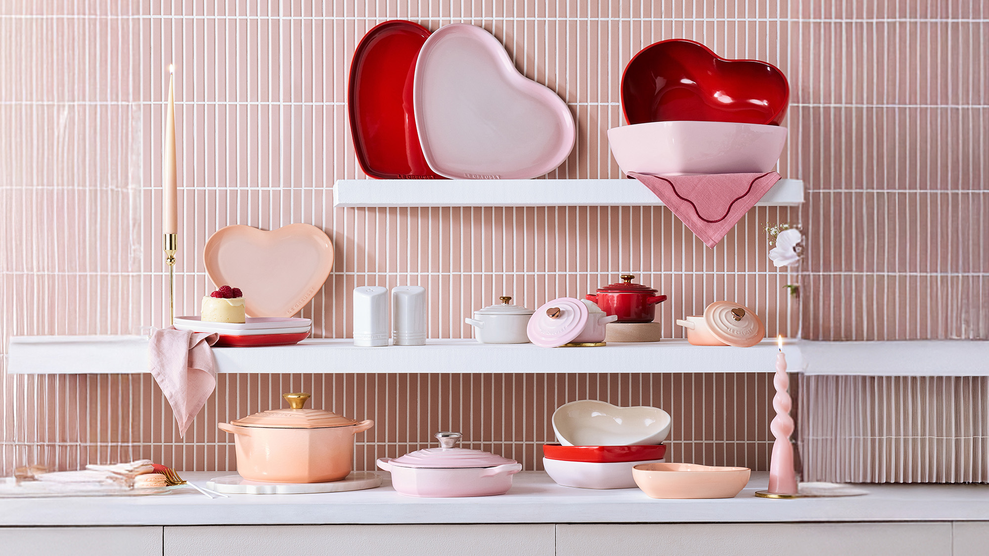 A kitchen with heart-shaped cookware on shelves against a pink tiled wall, featuring pastel and red accents.