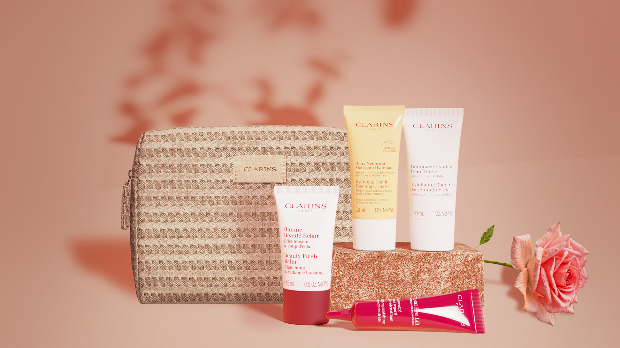Skincare products with a woven cosmetic bag and a pink rose on a soft pink background.