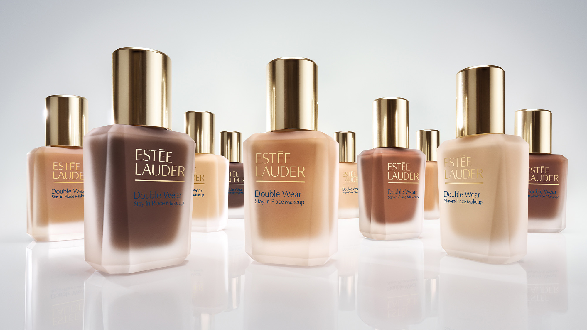 Bottles of Estée Lauder Double Wear foundation in varying shades, arranged on a reflective surface.