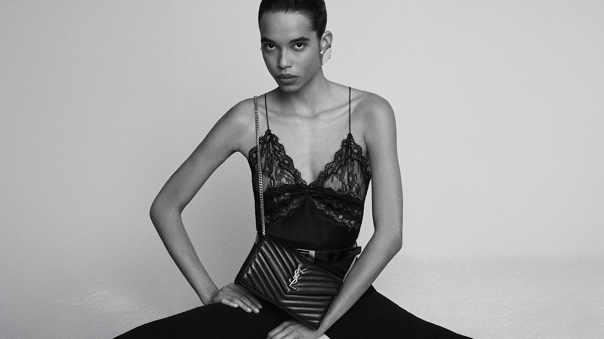 Model in lace top holds quilted YSL bag; earrings visible. Black and white.