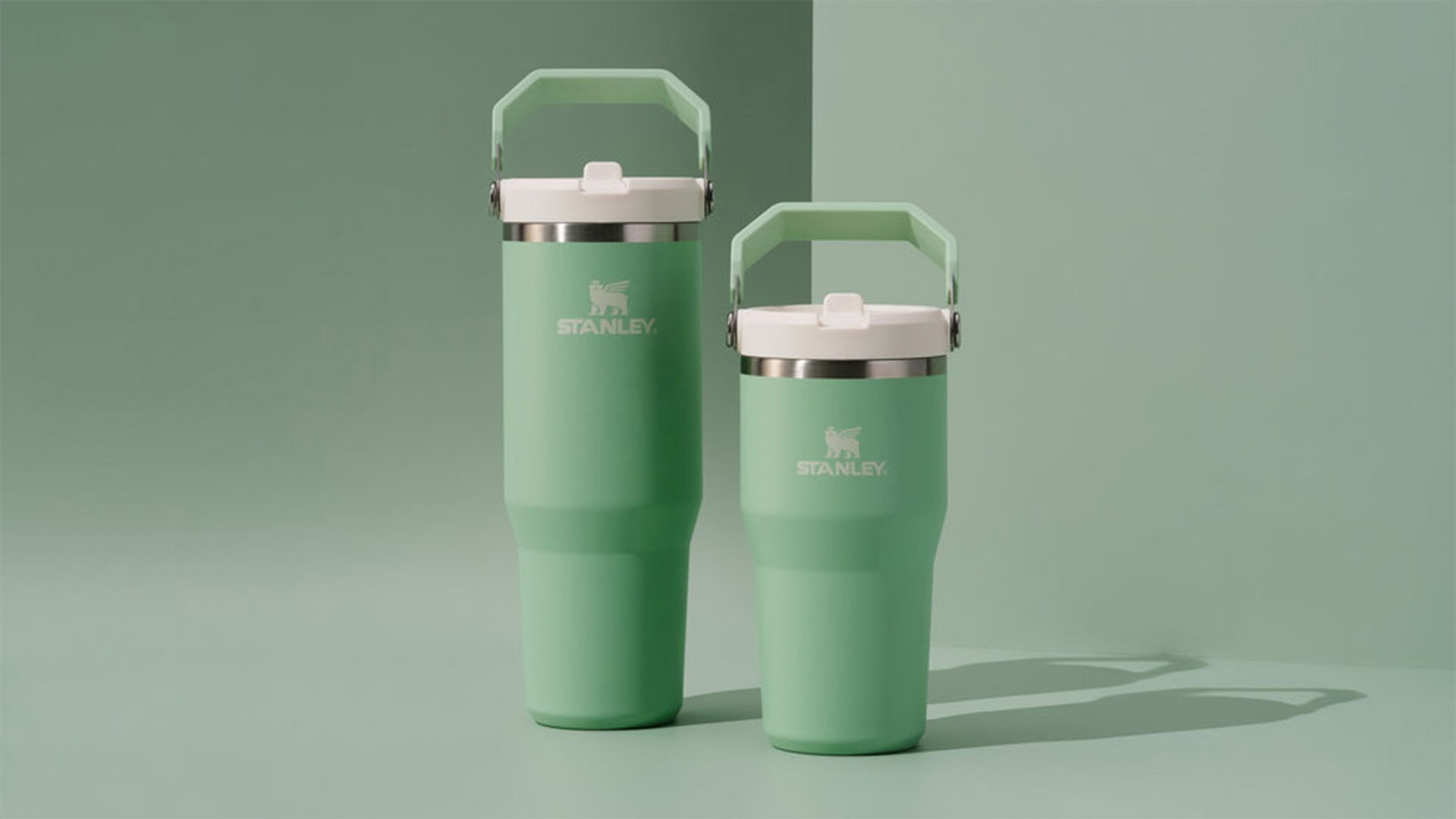 Two green travel mugs with handles on a light green background.