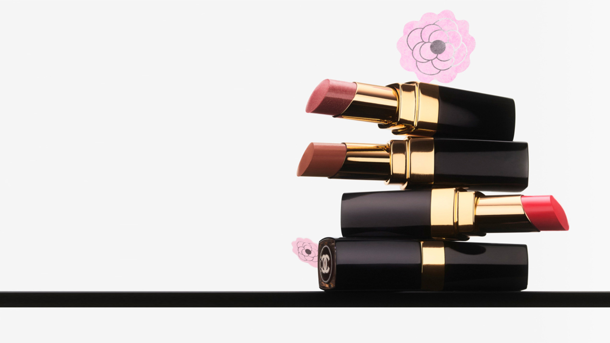 Three lipsticks stacked horizontally with pink floral decorations in the background.