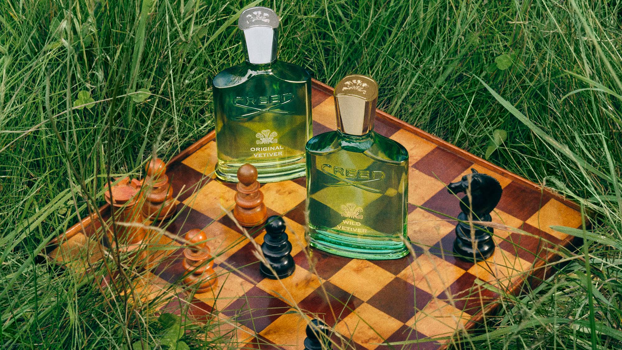 House Of Creed perfumes on a chessboard surrounded by grass.