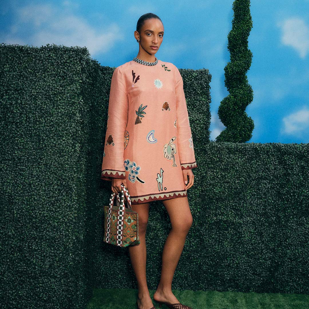 Woman in peach shift dress with nature motif, chain necklace and patterned handbag