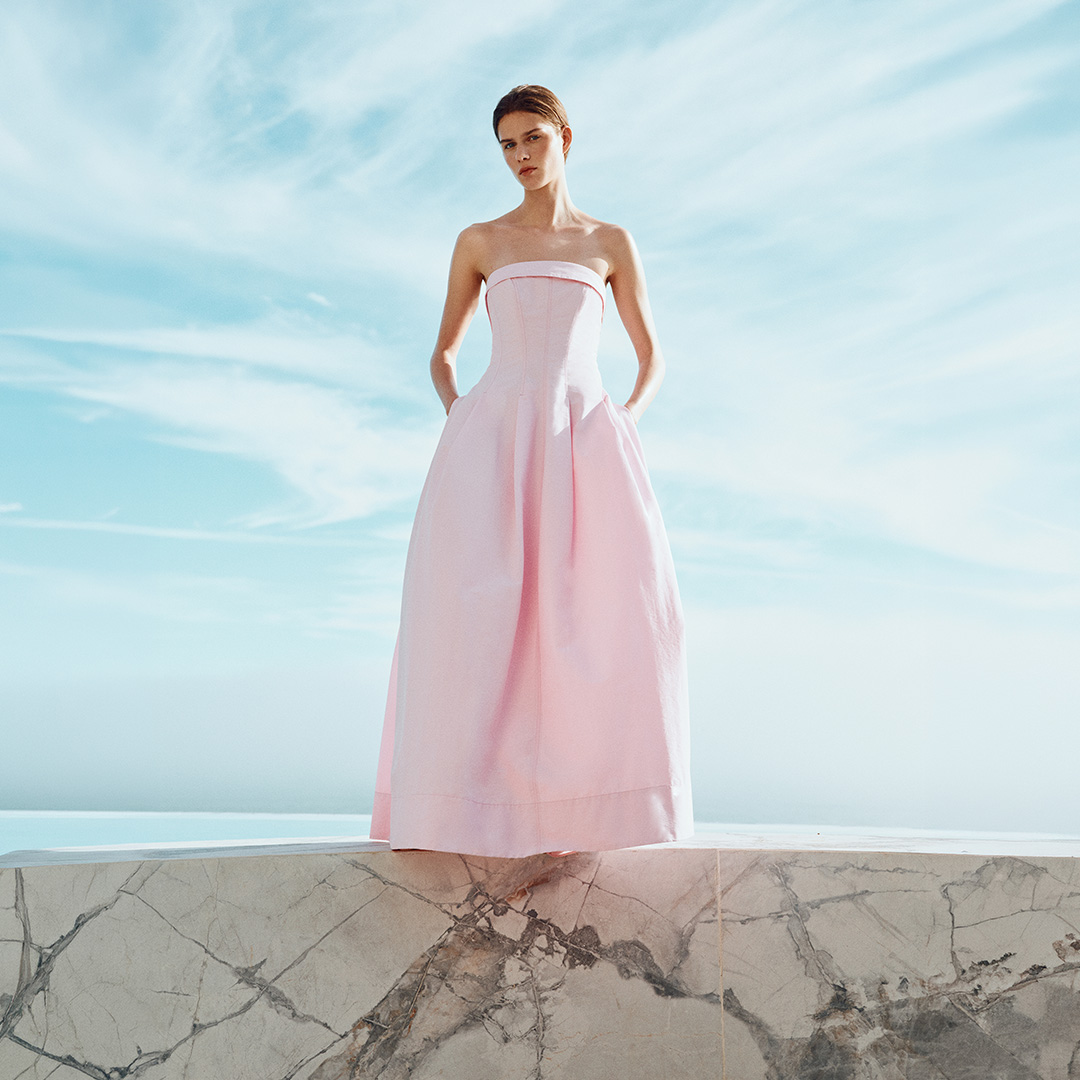 Woman in pale pink strapless ball gown on marble platform with turquoise sea and sky backdrop