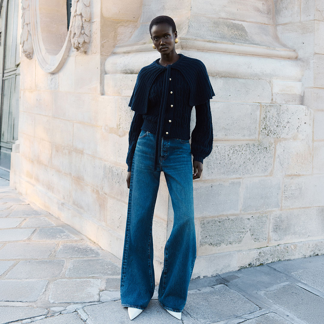 Woman wearing blue denim jeans and dark navy pinstriped button-up jacket with gold hoop earrings