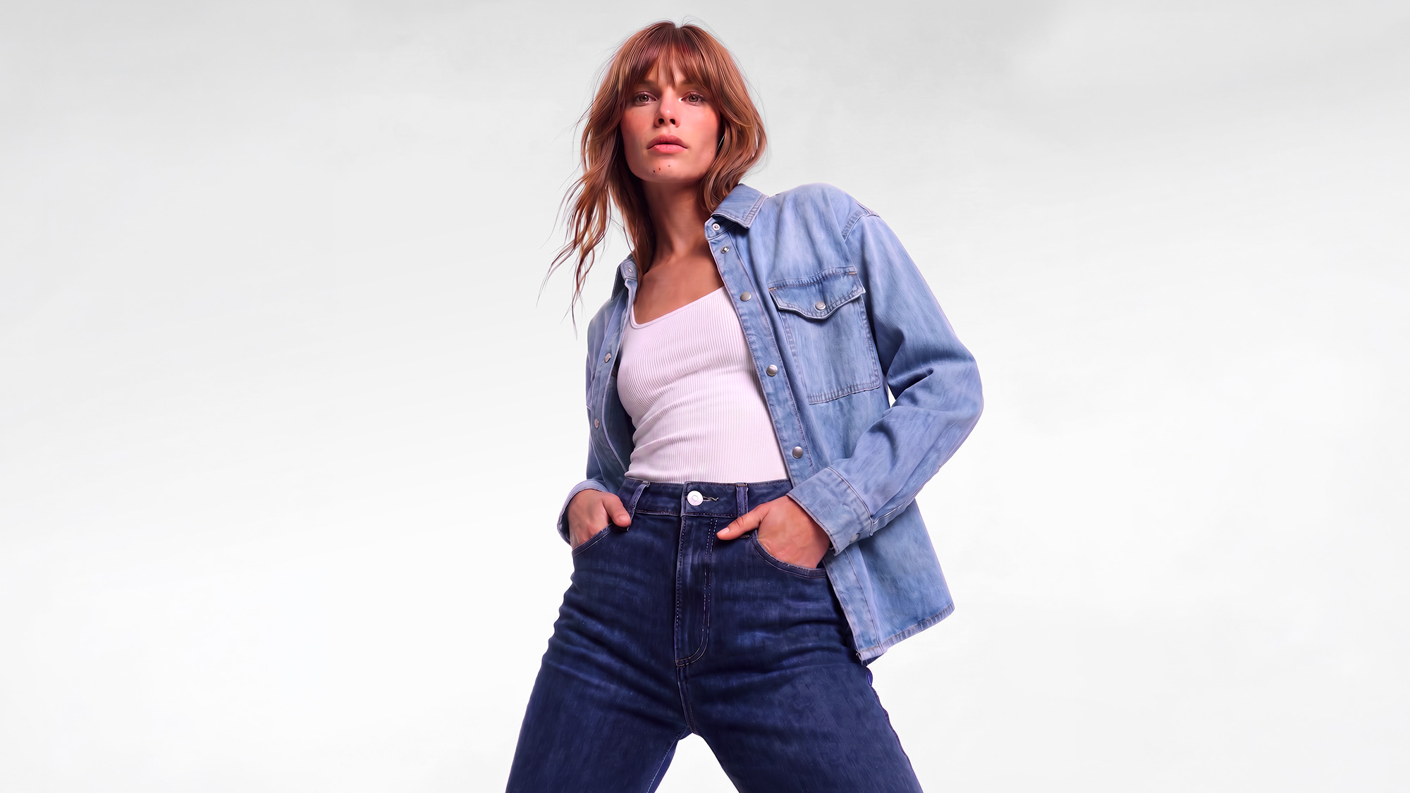 Woman wearing light blue denim jacket over pink ribbed top with dark blue jeans