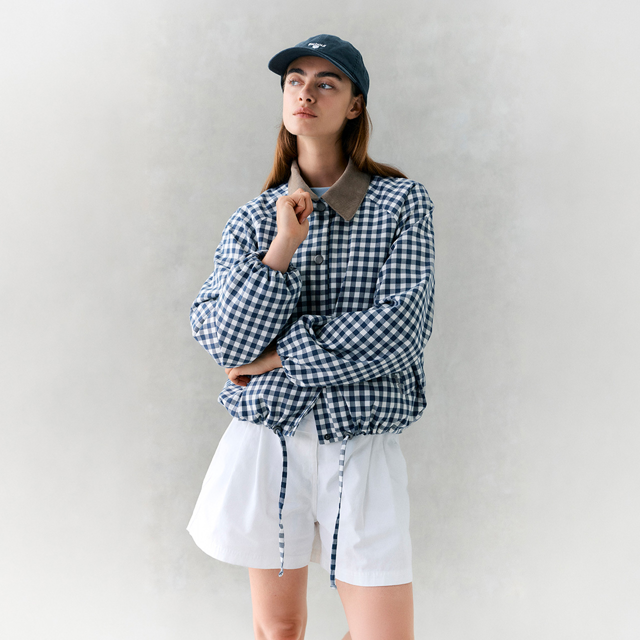 Woman wearing navy gingham shirt with grey collar and white skirt, styled with navy cap