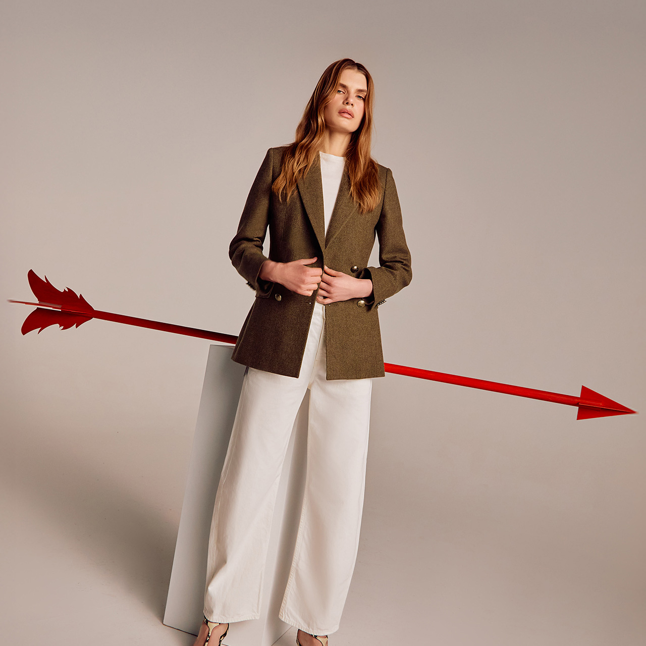 A woman in a blazer and wide pants stands with a large, red, 3D arrow behind her.