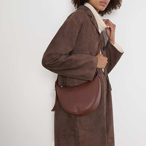 Person wearing a brown coat, carrying a brown curved handbag, and wearing a white turtleneck underneath.
