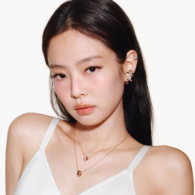 A person wearing elegant Chanel earrings and a necklace, posing in a white top against a plain background.