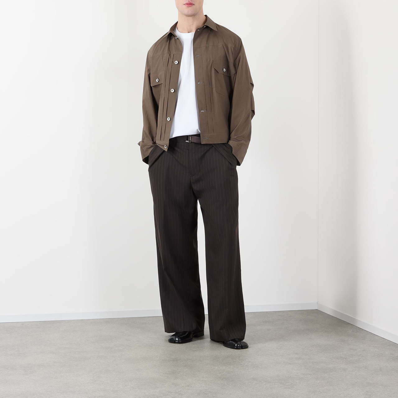 Menswear model wearing brown jacket, pint stripe trousers and white t-shirt, pockets with hands in the pockets