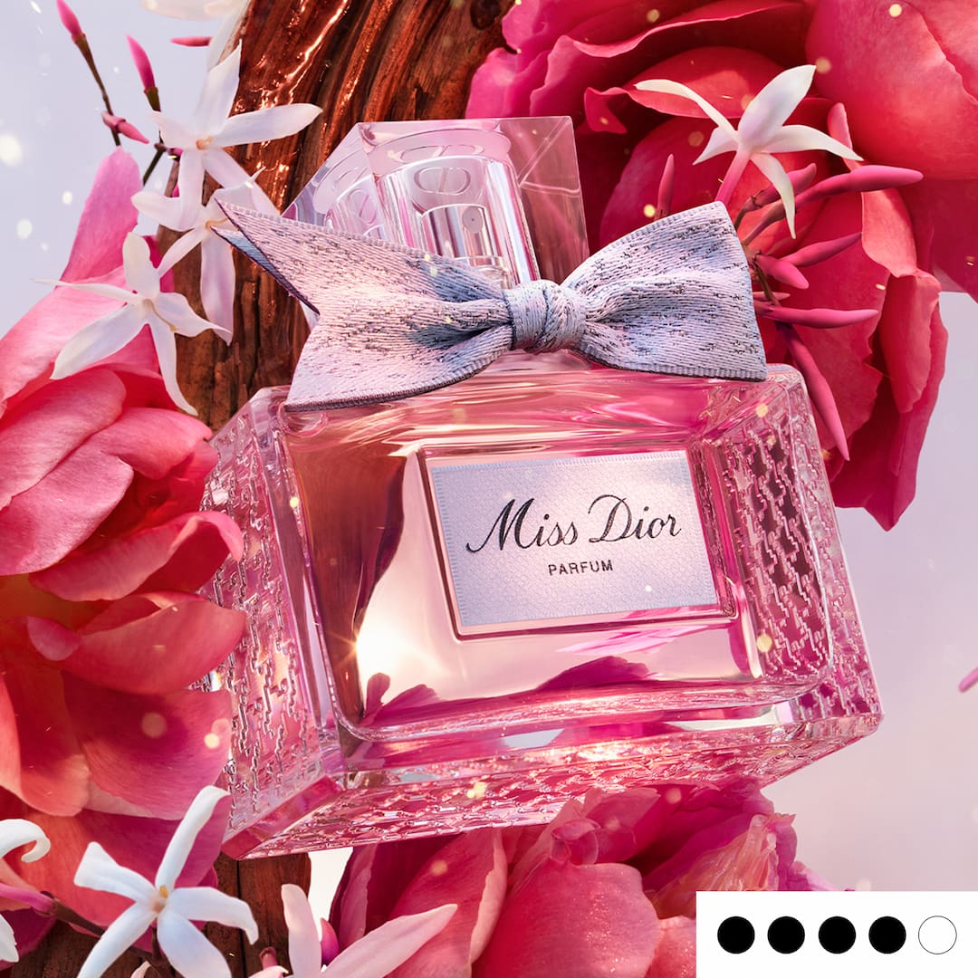 Perfume bottle with a bow amid pink and white flowers, labeled 'Miss Dior Parfum.'