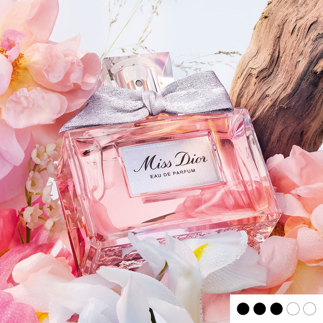 A bottle of Miss Dior Eau de Parfum surrounded by pink and white flowers, with a silver bow on the cap.
