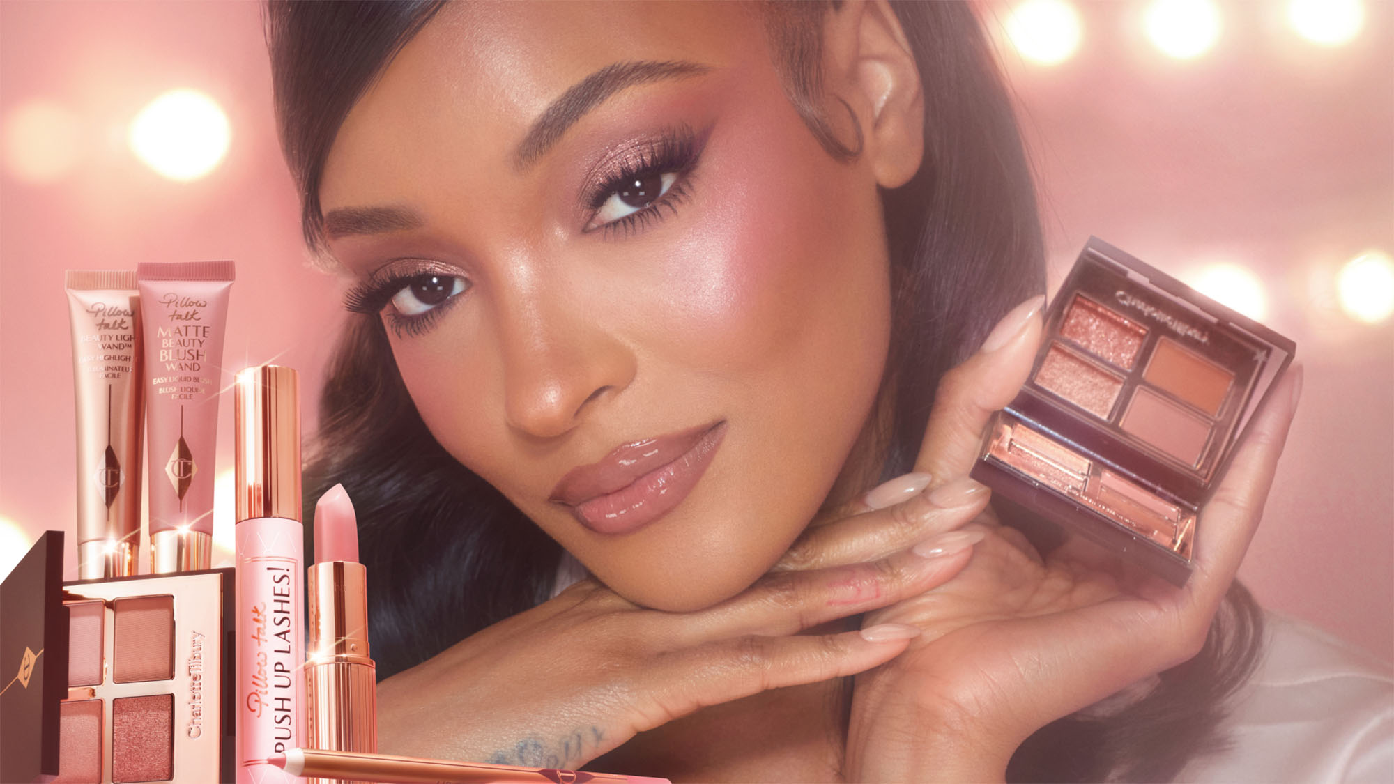 A person poses with makeup products, featuring pink eyeshadow and lipstick. The background is softly lit, creating a glamorously lit effect.