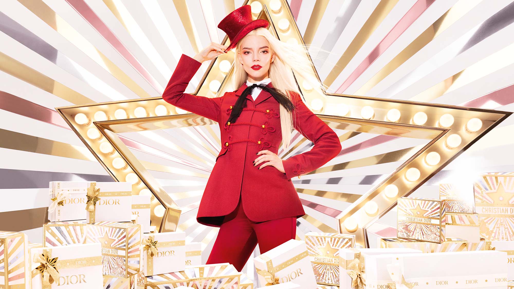A woman in a red outfit poses with a top hat in front of a star, surrounded by Dior gift boxes.