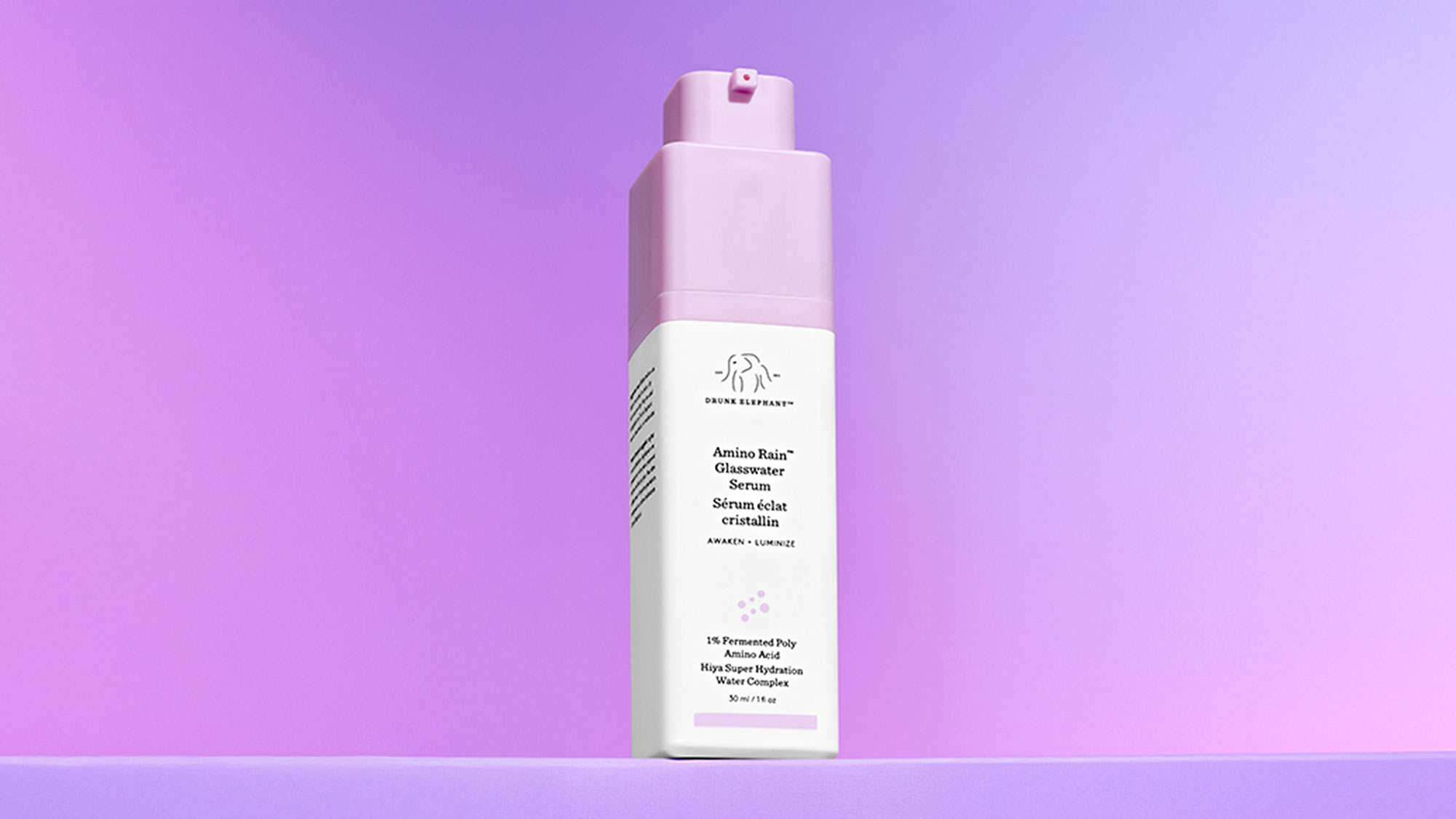 A pink and white skincare serum bottle stands against a gradient purple background.