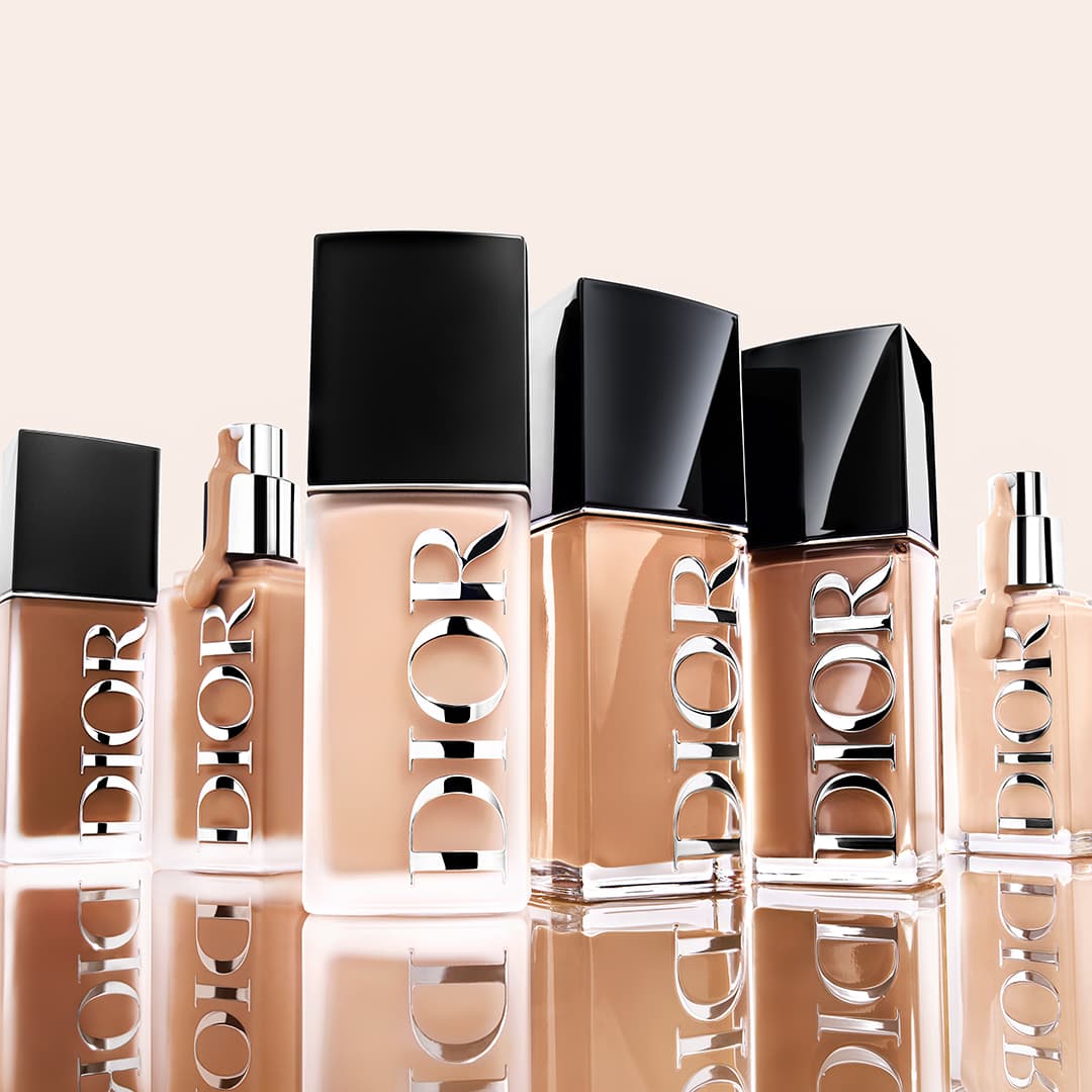 A lineup of Dior foundation bottles with black caps displayed on a reflective surface.