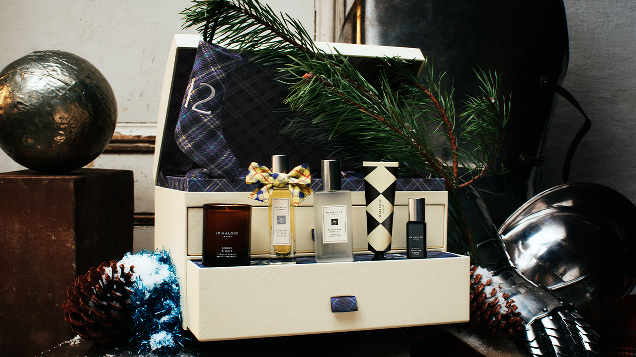 Cream luxury gift trunk with assorted fragrances, gold bow, festive decorations and evergreen sprigs