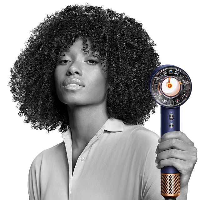 A person with curly hair holds a modern hairdryer.