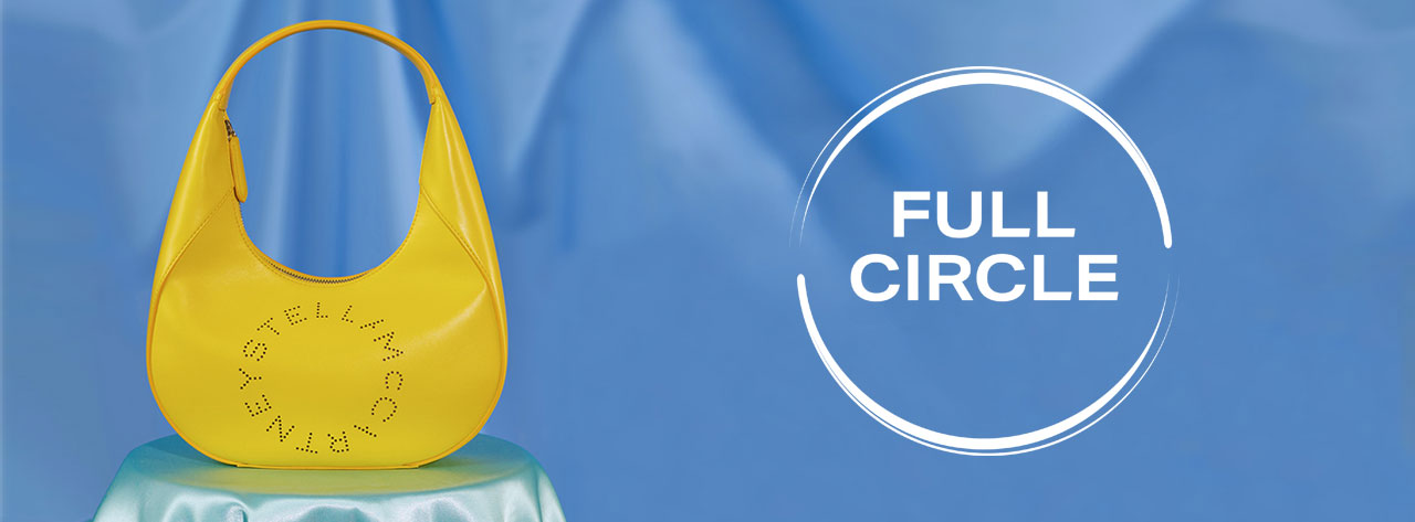 A black handbag with large gold and silver chain straps is displayed on a speckled surface. The words 'FULL CIRCLE' are printed in a white circle.