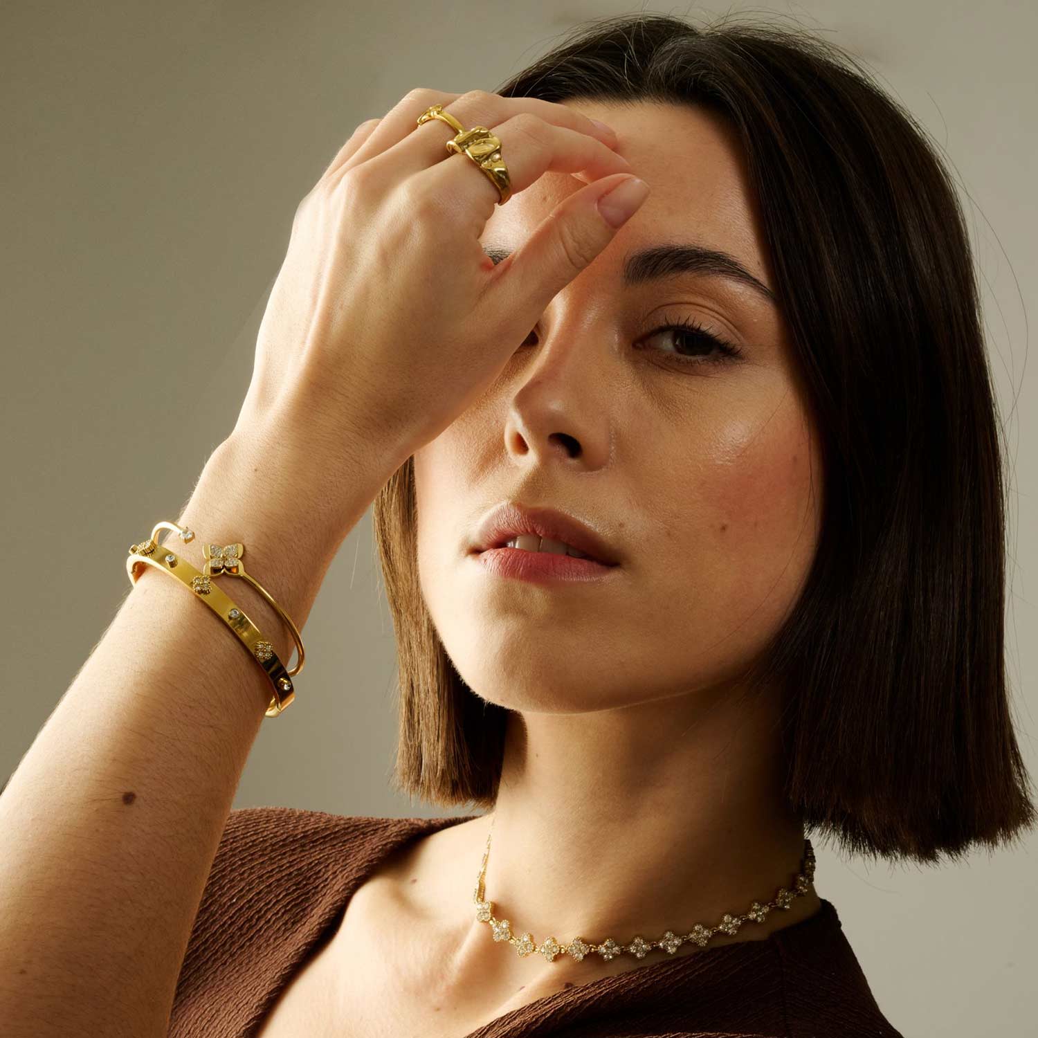 Hands with colorful, jeweled rings and bracelets over a red fabric background.