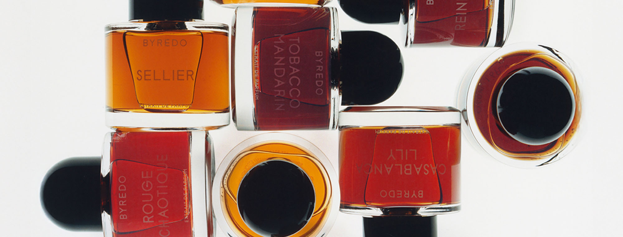 Assorted bottles of Byredo perfumes with black caps, featuring amber and red-toned liquids.