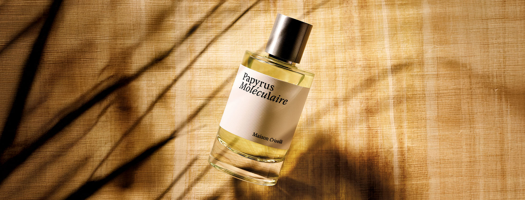 Perfume bottle labeled 'Papyrus Moléculaire' by Maison Crivelli on a textured surface with shadow patterns.
