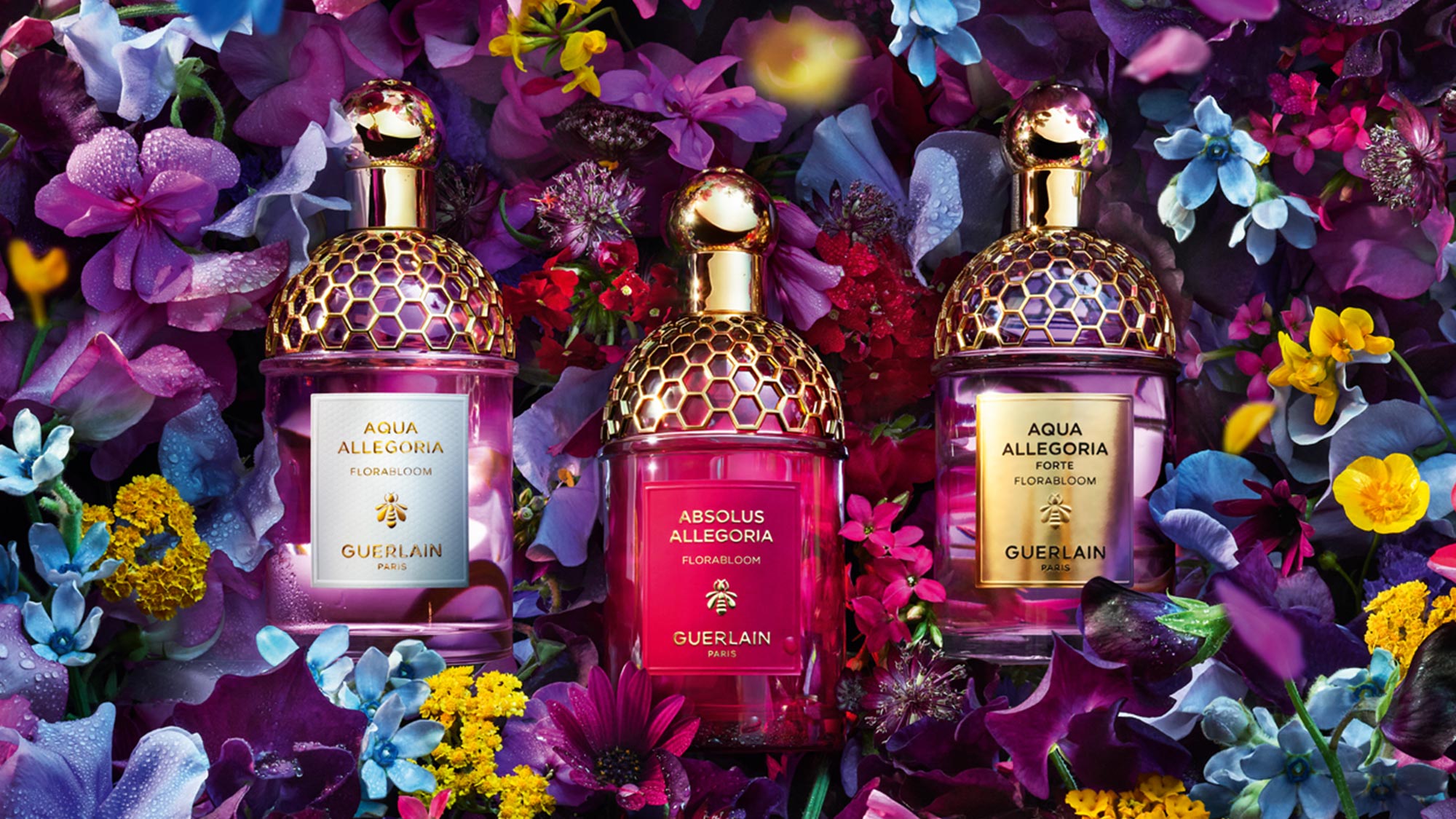 Three Guerlain perfume bottles surrounded by a variety of colorful flowers.