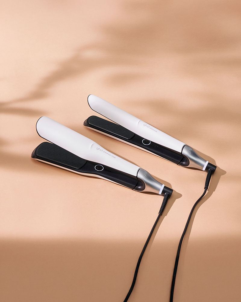 
Two white and black hair straighteners with cords on a beige background.