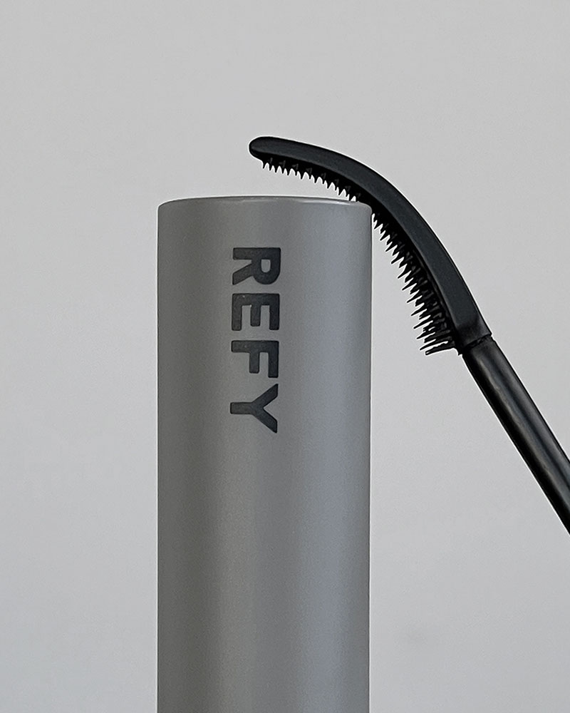 
A gray cylindrical container labeled 'REFY' with a curved black applicator featuring fine bristles.

