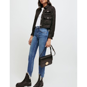Model wearing Maje Pachabfran Mid-Rise Slim Ripped Hem Jeans in blue denim, styled with black cropped tweed jacket and black shoulder bag