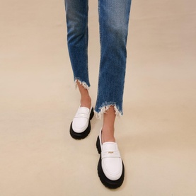 Model wearing Maje Pachabfran Mid-Rise Slim Ripped Hem Jeans in blue denim with frayed hem, styled with white loafers