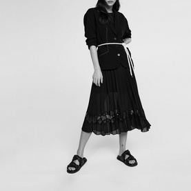 Model wearing Claude Pierlot Teli Pleated Midi Dress in black, styled with a black jacket, white belt and black chunky sandals