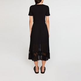 Model wearing Claude Pierlot Teli Pleated Midi Dress in black, back view, with sheer lace hem detail and short sleeves