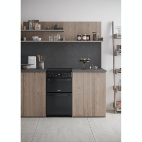 Hotpoint Electric Freestanding Double Cooker in black, set into light wood kitchen cabinetry with marble-effect splashback and open shelving above