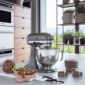 KitchenAid 4.8L Artisan Stand Mixer in grey with polished bowl, styled in a modern kitchen with herbs and stacked bowls nearby