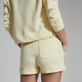Model wearing Reiss Annie Jersey Shorts in yellow, styled with a matching yellow sweatshirt. Back view showing cuffed hem and pocket detail