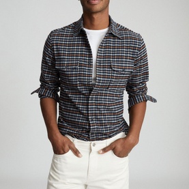 Model wearing Reiss Ash Overshirt in blue plaid check, styled with a white tee and white jeans, sleeves rolled up