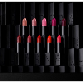 NARS Audacious Lipstick collection displayed in a grid formation against a dark branded backdrop, featuring multiple shades including Barbara