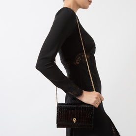 Model carrying Alexander McQueen Skull Clutch Bag in black croc-effect leather with gold chain strap, worn crossbody