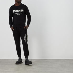 Model wearing Alexander McQueen Graffiti Logo Sweatpants in black, styled with matching black sweatshirt and black boots
