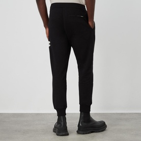 Model wearing Alexander McQueen Graffiti Logo Sweatpants in black, ribbed cuffs, rear view, styled with black chunky-sole boots