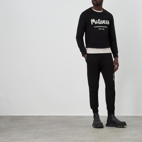 Model wearing Alexander McQueen Graffiti Logo Sweatpants in black, styled with matching black graffiti logo sweatshirt and black chunky boots