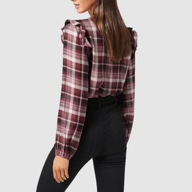 Model wearing Forever New Amy Checked Frill Shoulder Blouse in burgundy check, styled with black high-waisted trousers. Back view shown