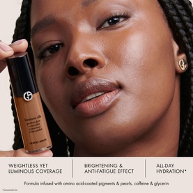 Model with ARMANI BEAUTY Luminous Silk Lightweight Liquid Concealer applied to under-eye area, shown with product bottle in hand
