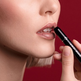 Model wearing Armani Beauty Color Sketcher lipstick in Sepia, shown applying the black bullet lipstick to lips close-up